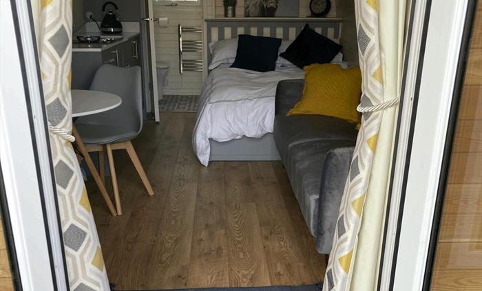 showing inside of pod from door, made up bed, kitchenette, sofa and bathroom